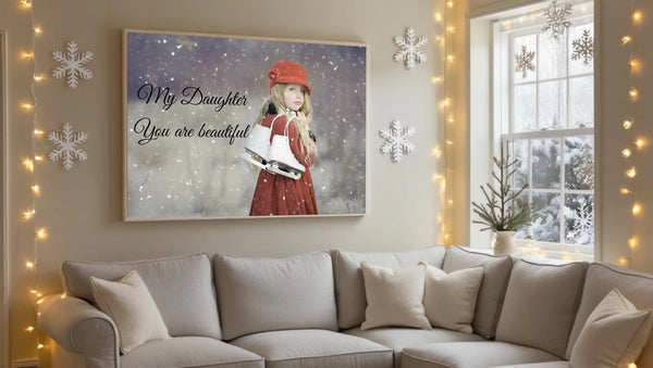 A cozy winter-themed living room with a soft, neutral color palette. Above a light gray or beige sofa, there is a large blank canvas frame hanging on the wall. The room features seasonal decorations such as snowfla